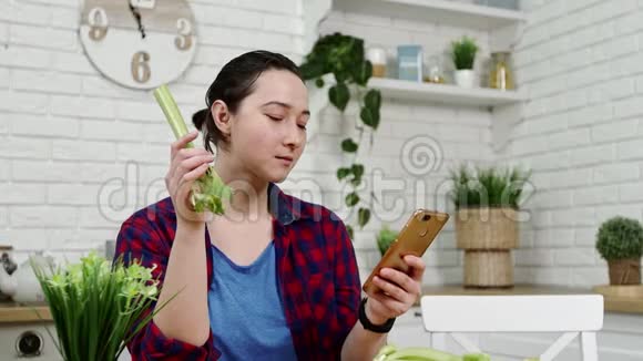 手拿智能手机的女人在厨房吃芹菜视频的预览图