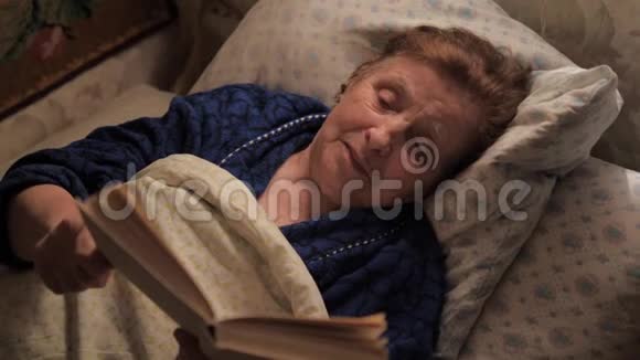 一位老妇人躺在毯子下面的床上看书视频的预览图