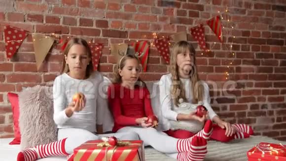 三姐妹穿着柔软的睡衣坐在床上玩着红苹果卧室装饰着圣诞节视频的预览图