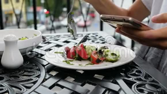 女人把蔬菜沙拉放在盘子里在餐馆吃饭时用电话视频的预览图