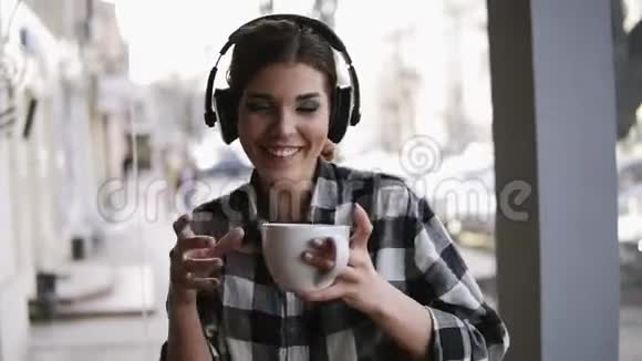快乐有趣的年轻女孩听着耳机里的音乐手里拿着一杯咖啡跳舞模糊的街道视频的预览图