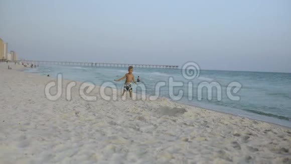 一个快乐的小男孩沿着海滩奔跑微笑着视频的预览图
