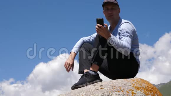 坐在石头上用电话看摄像机的人视频的预览图