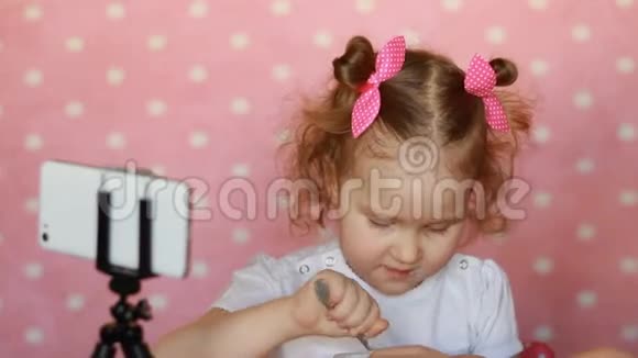 小女孩吃东西在智能手机上看卡通婴儿和小工具应用程序互联网游戏视频的预览图