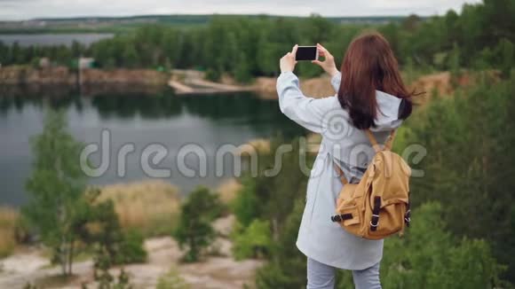 带背包的女旅行者用智能手机从悬崖上拍摄美丽景色的慢镜头肖像视频的预览图