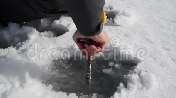 高加索人用冰螺钉在冰冻的湖面上钻冰快关门身体部分视频的预览图