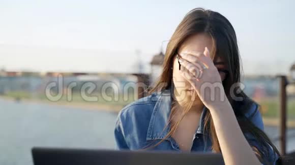 戴眼镜的漂亮年轻女子在户外咖啡馆的笔记本电脑上工作视频的预览图