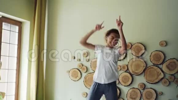 快乐的非洲裔美国青少年在卧室的床上听音乐跳舞和唱歌的慢动作视频的预览图