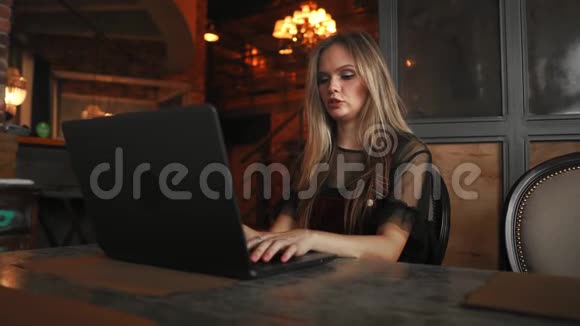 侧视年轻的商务女性坐在桌子旁在笔记本上做笔记桌子上有笔记本电脑智能手机和一杯视频的预览图