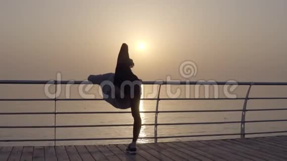 强壮而美丽的女人倚在横梁上温暖起来把她的腿横在后面灵活性海滨视频的预览图