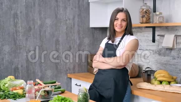穿着围裙在厨房摆姿势的幸福年轻女子有着积极的情绪视频的预览图