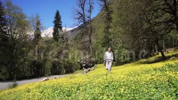 在夏日年轻女子踏着盛开的花朵走在绿色的田野上视频的预览图