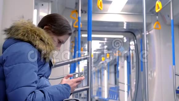 女人坐在一辆空的地铁车里在她的智能手机上看视频侧视视频的预览图