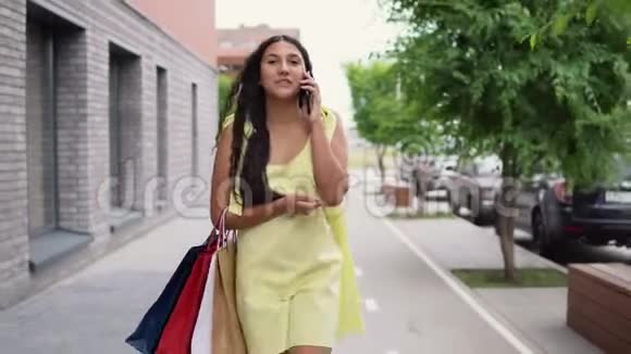 一个穿着长裙的年轻女孩在购物和打电话后在城市里走来走去4K视频的预览图