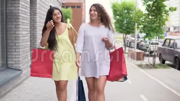 两个漂亮的女孩走在街上购物后手里拿着包裹心情很好4K视频的预览图