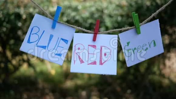 纸用手写字颜色蓝色红色绿色挂在一根绳子上用木夹在自然视频的预览图