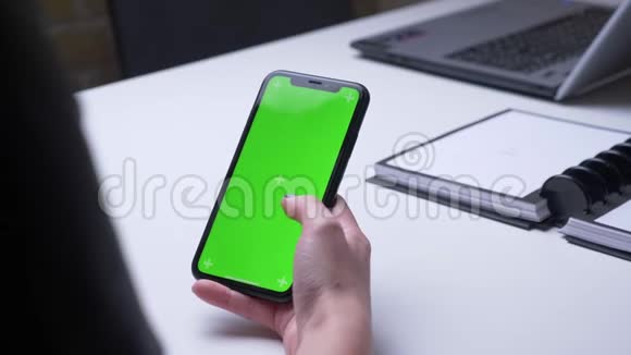 特写后景拍摄女性手在手机上滚动办公室内的绿色彩色屏幕在室内视频的预览图