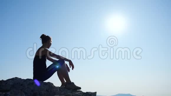 年轻受启发的女人坐在海面上一座山的顶部对抗美丽的蓝天快乐的剪影视频的预览图