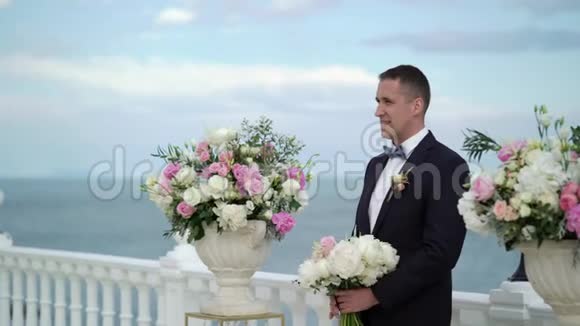 婚礼上的年轻新郎站在拱门的祭坛前等待新娘海边的婚礼视频的预览图