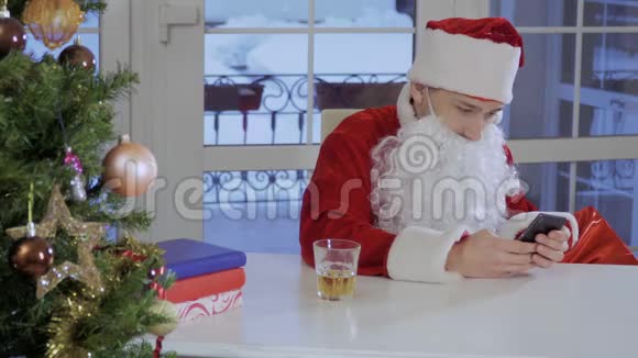 穿着圣诞老人服装的年轻人坐在桌子上在他的留言视频的预览图