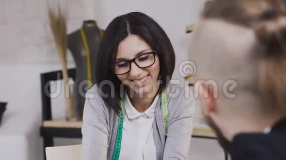 一个微笑的白种人裁缝的特写提供各种面料给她的客户在阿泰利埃商人拜访裁缝视频的预览图