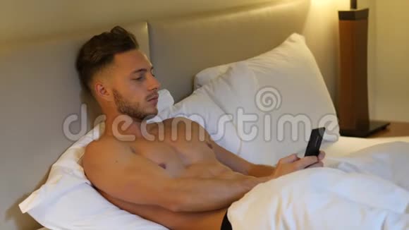 在床上打手机的肌肉发达的年轻人视频的预览图