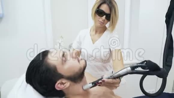 美容师金发留着短头发戴着特殊的眼镜进行激光脱毛手术将头发从视频的预览图