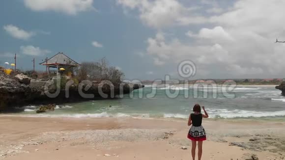 4K飞行无人机视频年轻女子在热带野生岩石海滩拍照巴厘岛视频的预览图