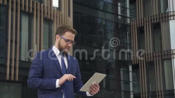 英俊的商人正在使用平板电脑站在办公楼的背景上视频的预览图