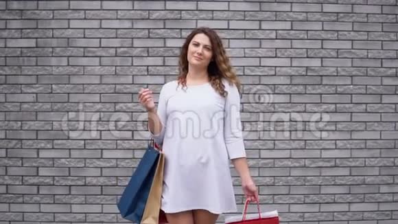 一个女孩穿着一件浅色连衣裙购物后带着一堵石头墙的背景心情很好慢动作视频的预览图