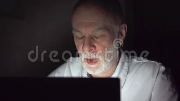 疲惫的资深商人深夜在笔记本电脑上工作劳累过度剧烈头痛视频的预览图