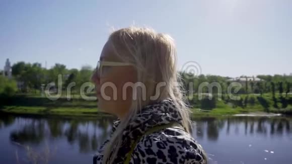 一个白发戴眼镜的女孩在河的高堤上摄像机拍摄成轮廓特写脸部视频的预览图