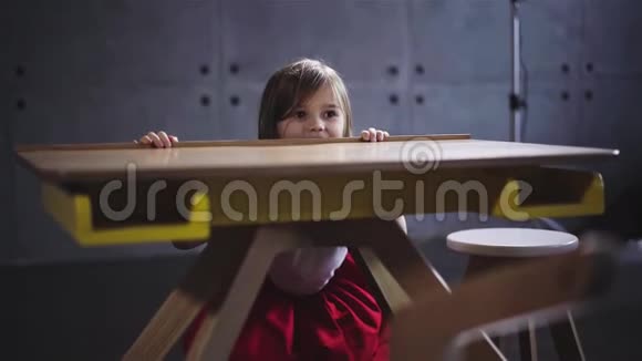 微笑的小女孩躲在木桌后面视频的预览图
