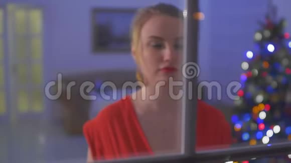 穿着红色连衣裙的漂亮吉尔尔走到窗前用手指触摸玻璃视频的预览图