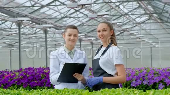 两个穿着白大褂黑围裙的女人科学家生物学家或农学家检查和分析花卉和绿色植物视频的预览图