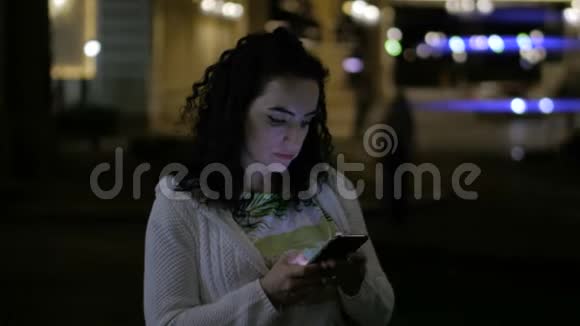 年轻女性在户外使用手机晚上打印短信在背景中可以看到夜晚城市的美丽灯光视频的预览图