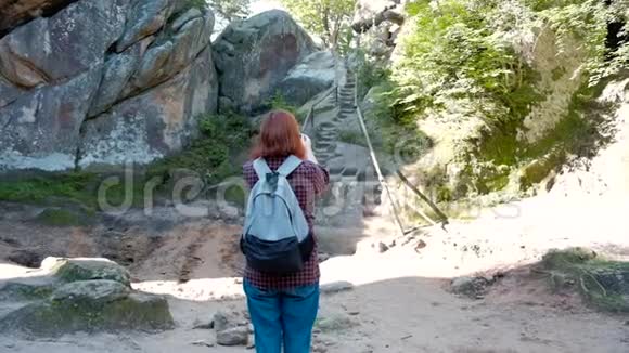 带背包的女旅行者用智能手机从悬崖上拍摄美丽景色的慢镜头肖像视频的预览图