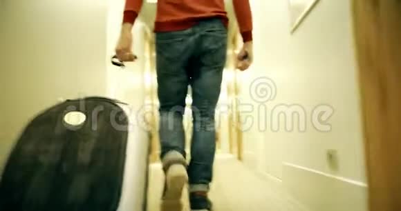 穿着牛仔裤和手提箱的男人沿着酒店走廊散步视频的预览图