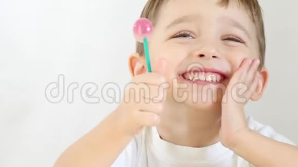一个快乐的孩子高兴地舔棒棒糖特写坐在一张桌子上的白色背景视频的预览图