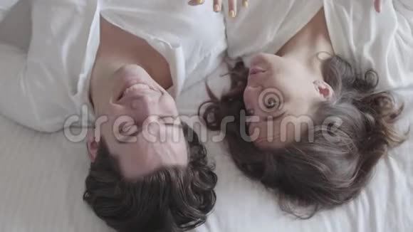 头顶射中幸福的年轻夫妇躺在床上谈特写俯视令人放松的男人和女人视频的预览图