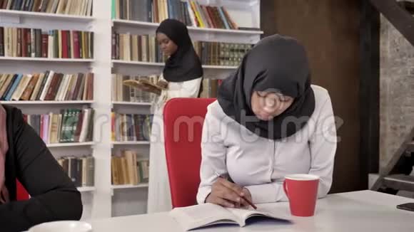 穆斯林青年妇女戴头巾在图书馆学习阅读和准备考试书架与书籍背景伊斯兰视频的预览图