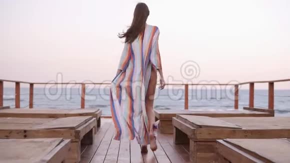 华丽的背面慢动作镜头一个穿着泳衣的白种人模特和夏季开衫走在木地板上视频的预览图