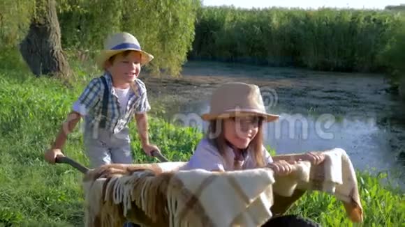 小男孩推着手推车小女孩在村里孩子们戴着草帽在湖里休息视频的预览图