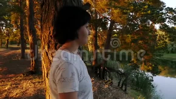 一个年轻的女人站在森林和河流背景上的一棵树附近视频的预览图