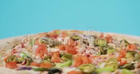 蓝色背景下旋转美味比萨饼与培根和蔬菜的特写视频的预览图