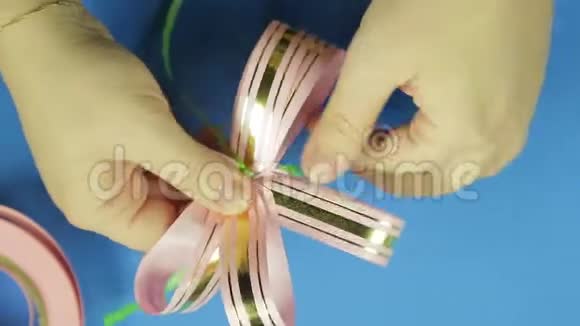女人手塑造粉红色丝带礼物蝴蝶结的花瓣蓝色背景视频的预览图
