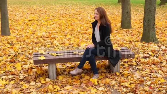 风平浪静的女人独自坐在秋天的公园里美丽的落叶视频的预览图