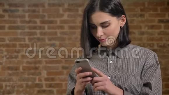 年轻漂亮的女人棕色短发在电话里发短信微笑砖墙背景视频的预览图