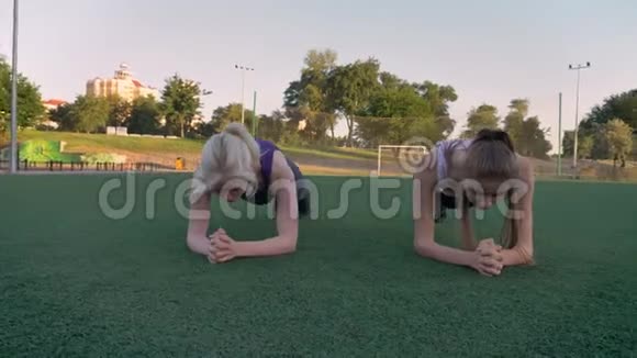 两个年轻漂亮的女人早上在公园的足球场上做木板运动减肥视频的预览图