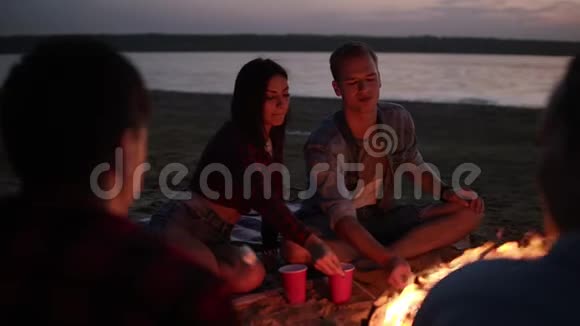 可爱的夫妇在篝火上烤棉花糖接吻年轻人坐在海滩上的朋友圈里视频的预览图